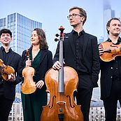 Das Foto zeigt das Eliot Quartett in Untersicht vor einer modernen Großstadt-Skyline