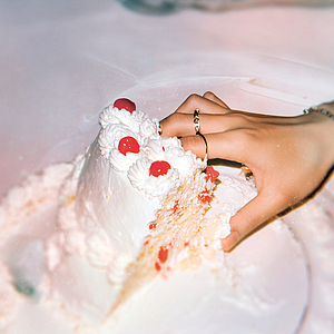 Das Foto zeigt eine Hand, die in eine Hochzeitstorte fasst.