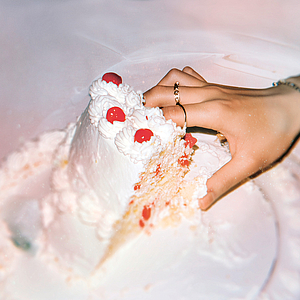 Das Foto zeigt eine Hand, die in eine Hochzeitstorte fasst.