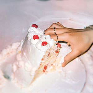 Das Foto zeigt eine Hand, die in eine Hochzeitstorte fasst.