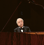 Das Foto zeigt den Pianisten Sir Andras Schiff von vorne, fotografiert vom Ende des braunen Flügels aus . Er spielt hingebungsvoll mit halb geschlossenen Augen