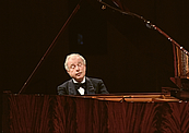 Das Foto zeigt den Pianisten Sir Andras Schiff von vorne, fotografiert vom Ende des braunen Flügels aus . Er spielt hingebungsvoll mit halb geschlossenen Augen