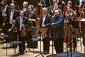 Das Foto zeigt dern Dirigenten Andris Nelsons, einige Musikerinnen und Musiker der ersten Geiden und der Celli. Sie stehen zum Publikum gewandt im Gewandhaus auf der Bühne und nehmen Applaus entgegen.