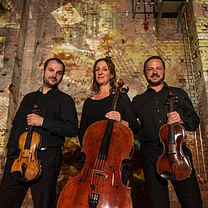Ariosa Trio steht vor einer Kirchenwand.
