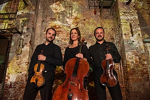 Ariosa Trio steht vor einer Kirchenwand.