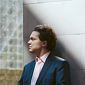 Das Foto zeigt ein Brusportrait des Pianisten Evgeny Kissin. Er steht ein wenig nach rechts aus der MItte des Bildes gerückt, trägt ein weißes Hemd, einen mittelblauen Blazer und schaut zur linken Seite. Hinter ihm erheben sich zwei unterschiedlich strukturierte Weiße Wände, die sich in der MItte treffen.