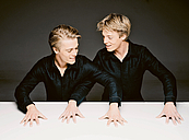 Das Foto zeigt die Geschwister Lucas und Arthur Jussen. Die Pianisten stehen nebeneinander an einer weißen Tischplatte auf die sie ihre Hände gelegt haben, als würden sie vierhändig KLavier spielen. Die mitteleren Arme sind überkreuzt. Beide tragen das gleiche schwarze Hemd.