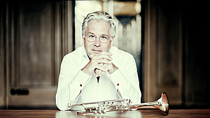 Portrait von Hakan Hardenberg. Er stützt seine Arme auf eine Tisch. Eine Trompete liegt vor ihm auf dem Tisch