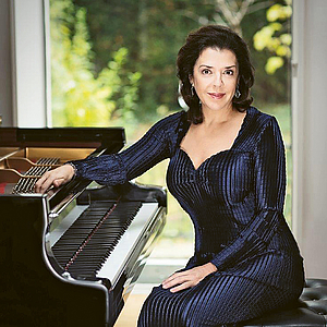 Die Pianistin Elena Bashkirova sitzt zur Kamera gedreht am Flügel, mit einer Hand auf den Saiten.