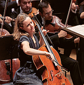 Das Foto zeigt eine Nahaufnahme der Cellistin Sol Gabetta im Gewandhaus, die leidenschaftlich ihr Instrument spielt. Im Hintergrund sind wneige Musiker des Gewandhausorchesters zu sehen.