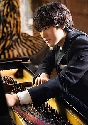Das Foto zeigt den Koreanischen Pianisten Yunchan Lim, der sich von er Klaviatur des Flügels her nach vorne in den geöffneten Glügel beugt und auf die Saiten schaut
